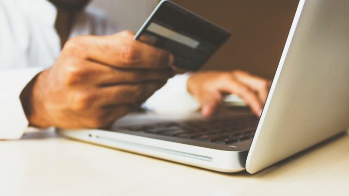 Dłoń trzymająca kartę kredytową przy laptopie — płatności i raty w sprzedaży kursów